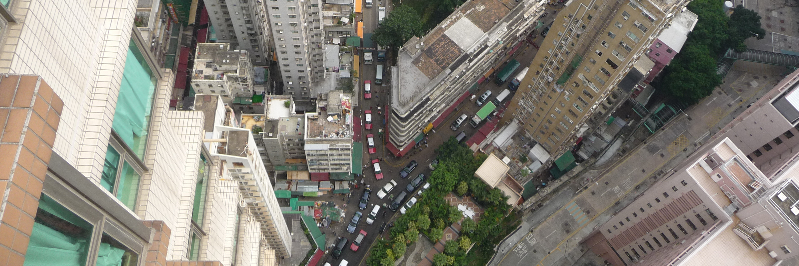 Blick vom Balkon eines Hochhauses in Hongkong senkrecht nach unten in die Straßenschlucht mit kleinen Autos
